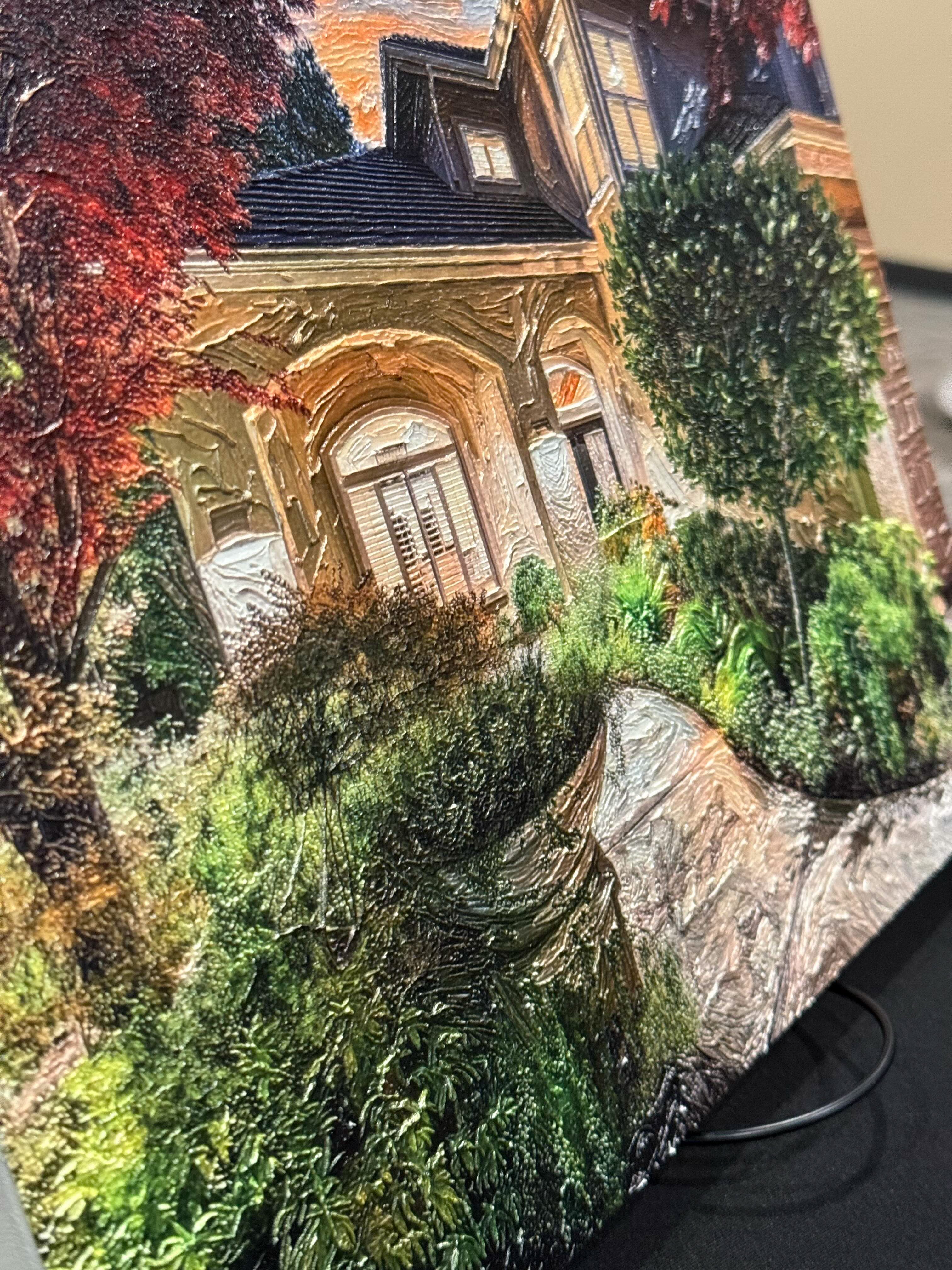A close-up of a canvas print or panel featuring a detailed painting of an old stone house with a garden path, surrounded by greenery and red autumn foliage.